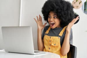 Excited African woman looking at laptop winning online, reading great news.